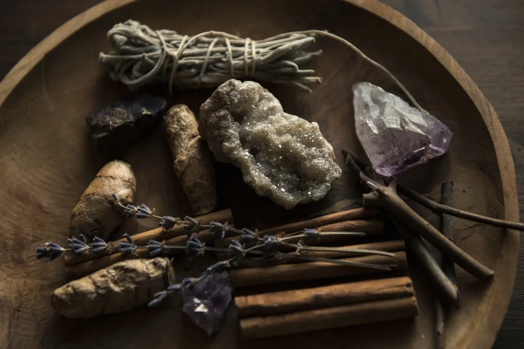 Collection of crystals, dry herbs including lavender, cinnamon sticks, and dried roots on wooden tray.